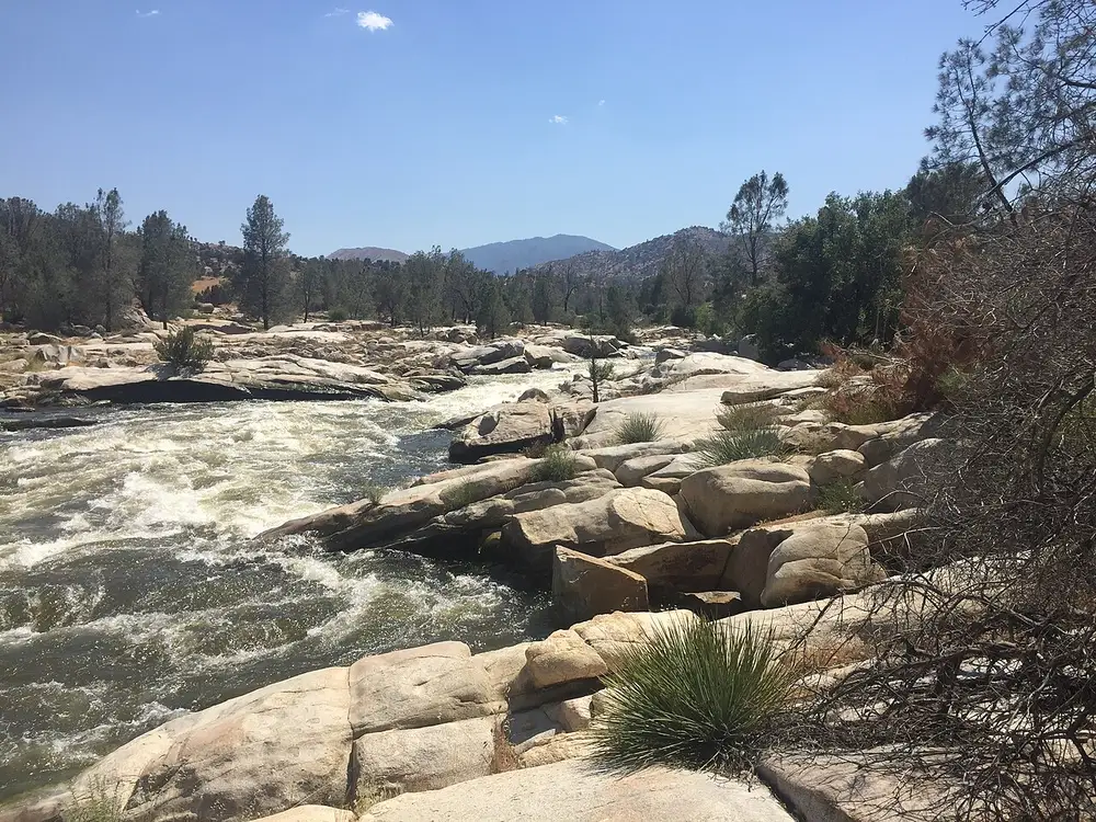 The Kern River rushing past big granite boulders under a blue sky