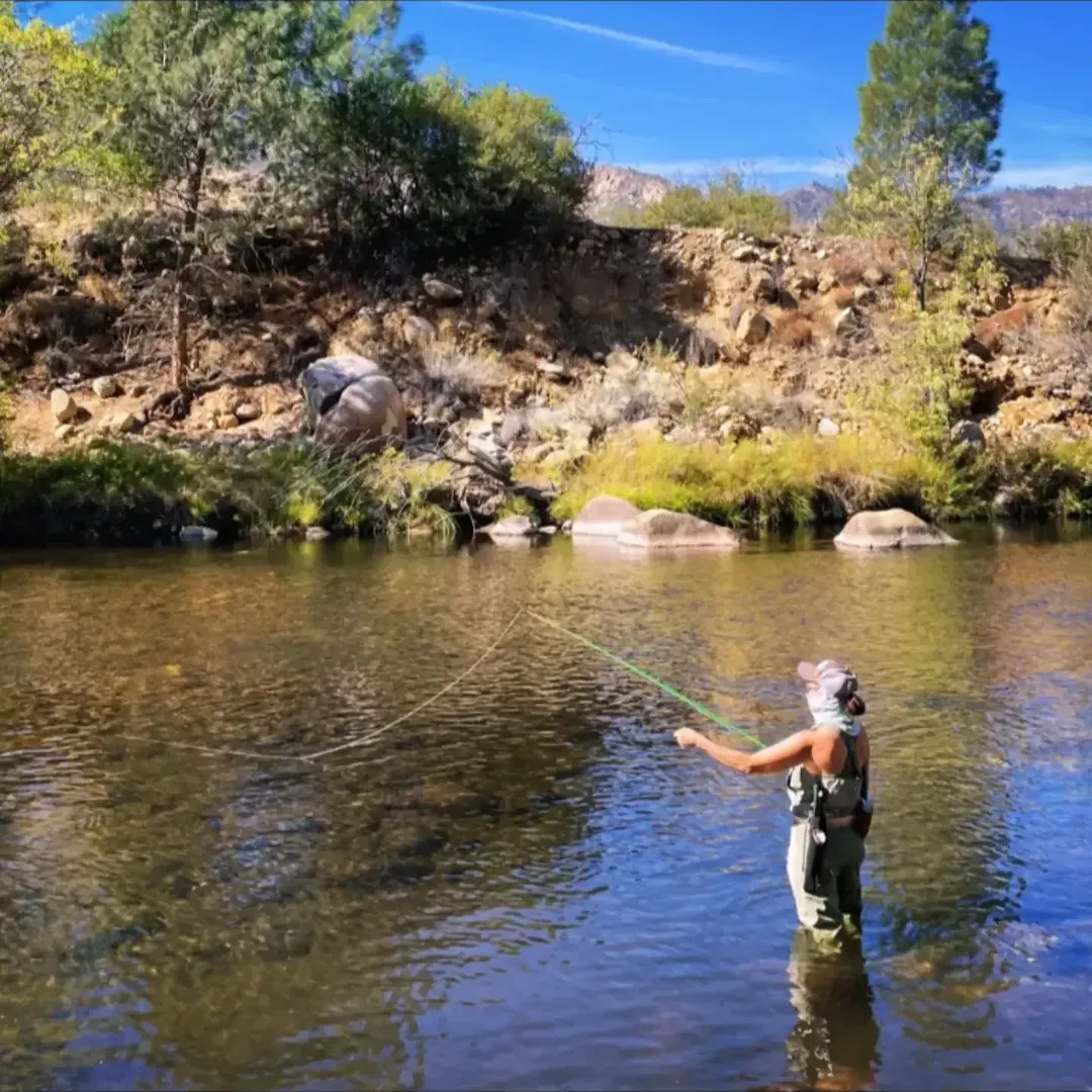 Krista standing in a clear mountain river, casting a fly fishing line