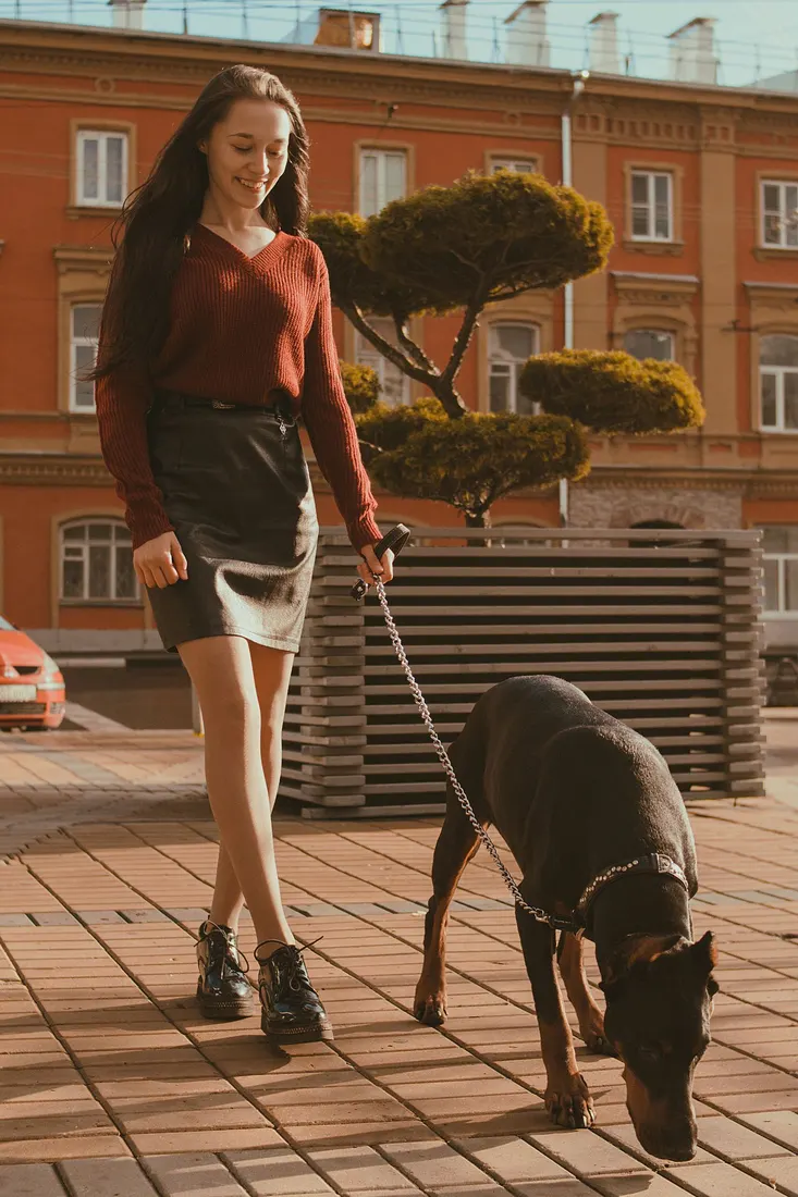 A woman walking her Doberman across a sunny city plaza