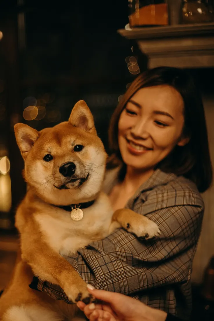 A smiling woman hugging her Shiba Inu at home