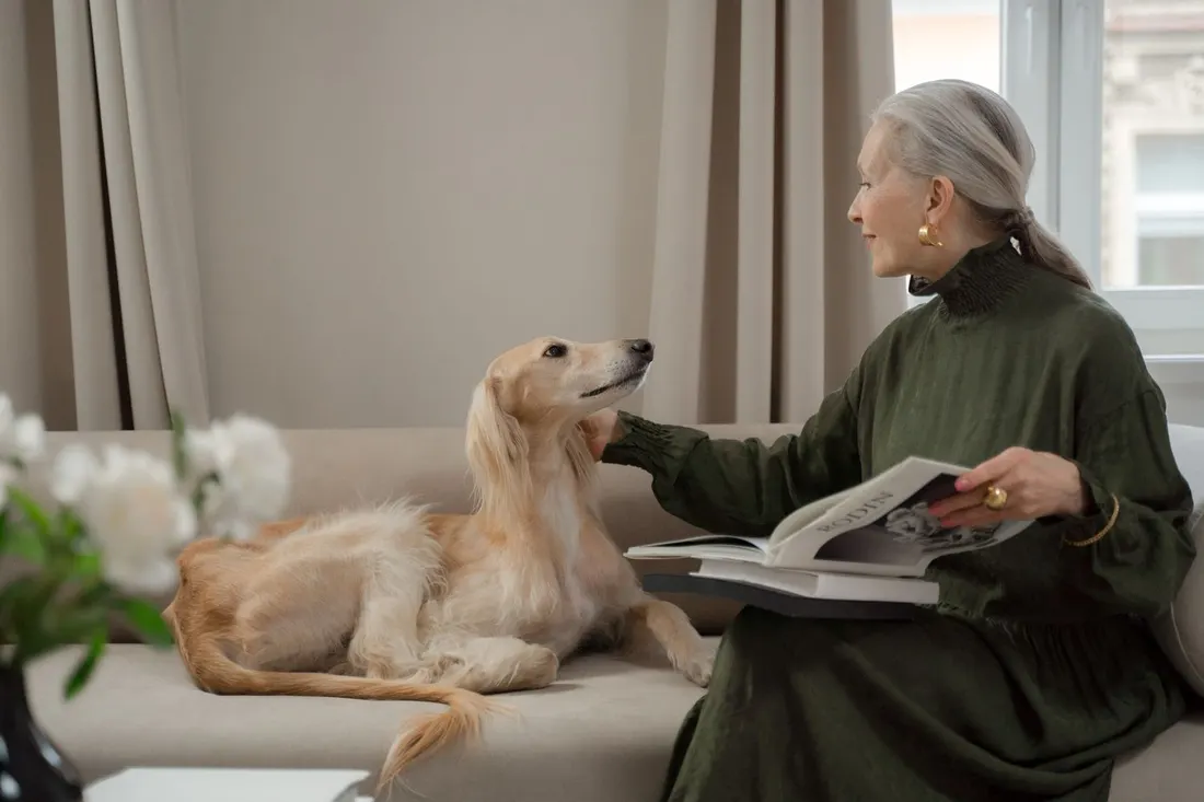A woman reading on a sofa at home while her calm golden dog rests beside her